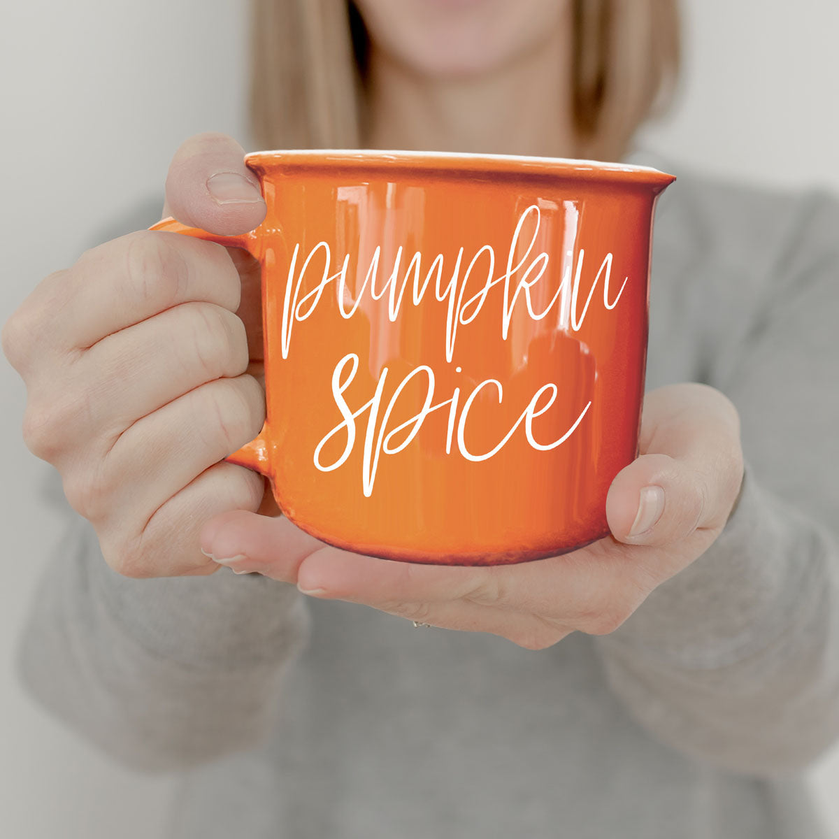 Orange mug with 'pumpkin spice' text held by a person