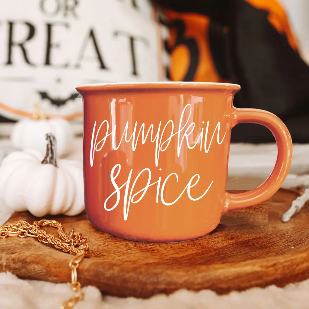 Orange 'Pumpkin Spice' mug on a wooden surface with Halloween decorations in the background.