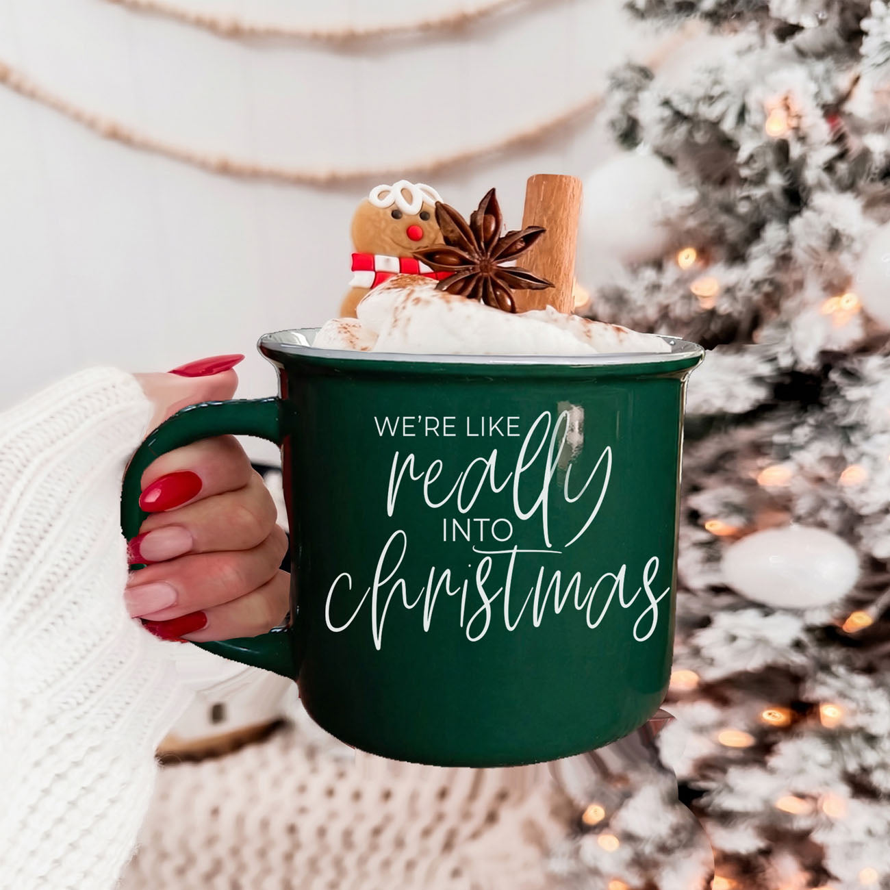 Green mug with 'We're like really into Christmas' text, held by a person, with festive background.