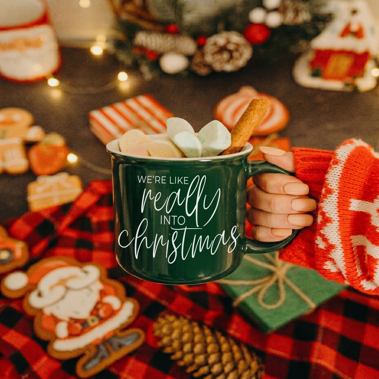 Person holding a mug with 'We're like really into Christmas' text, surrounded by holiday decorations.