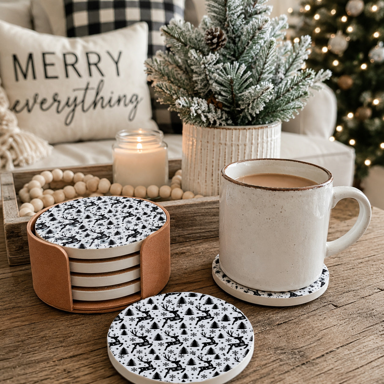 A set of ceramic coasters and matching cups with a black and white geometric pattern, styled on a wooden table in a cozy holiday setting with a mug of coffee, a candle, and a decorative pillow.