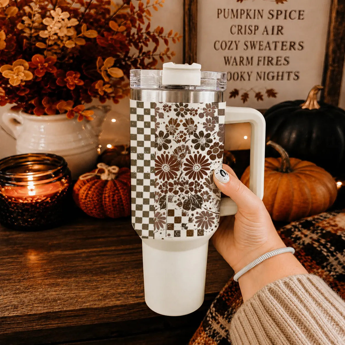Hand holding a patterned tumbler with autumn decor in the background