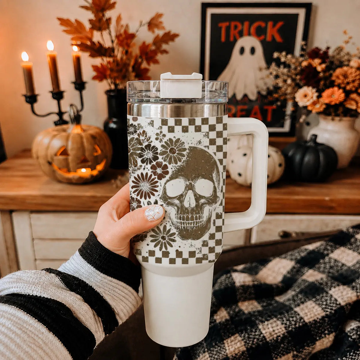 Person holding a white tumbler with a skull design in a cozy room decorated for Halloween.