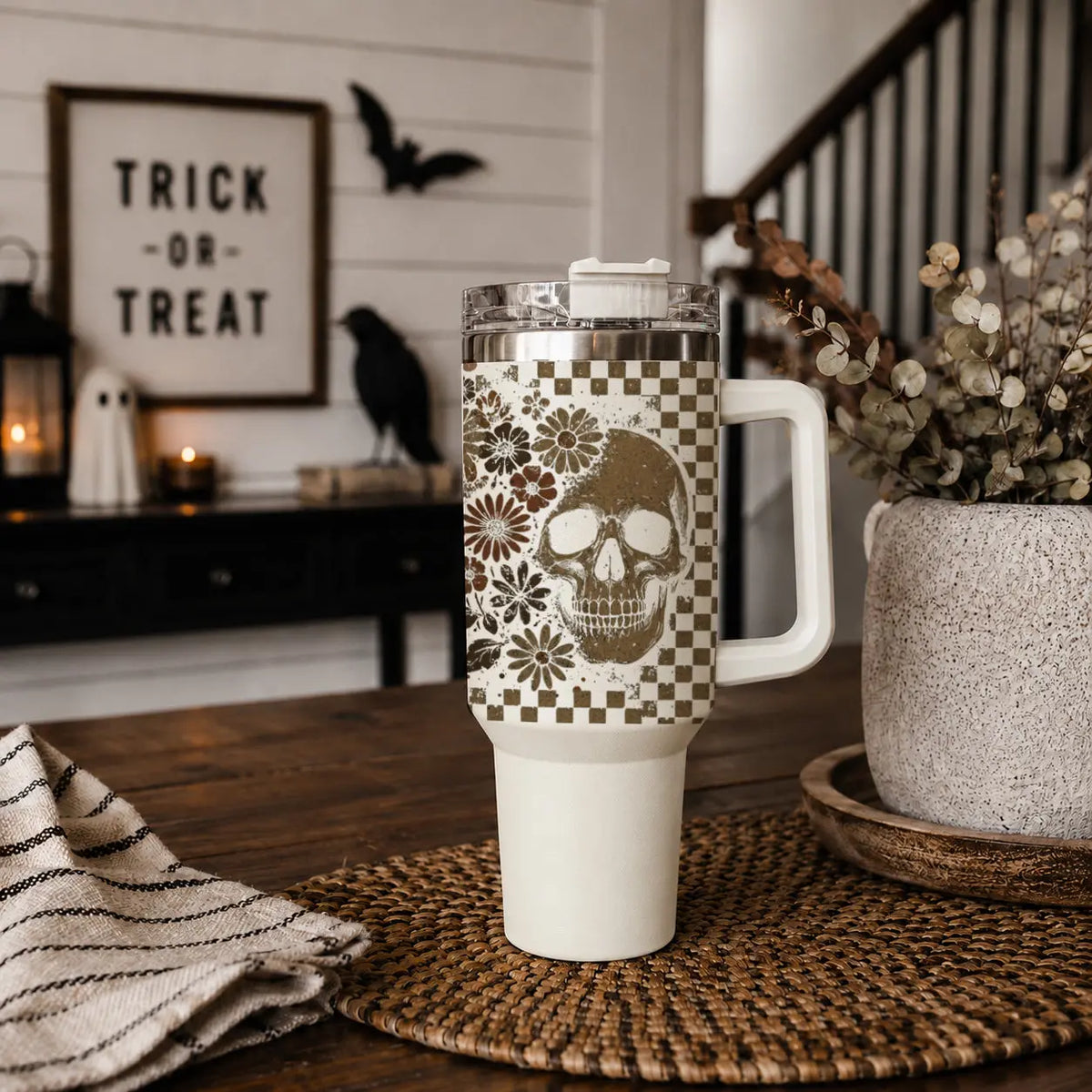 White tumbler with skull design on a wooden table with Halloween decorations in the background.