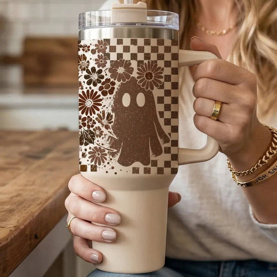 Person holding a beige tumbler with floral and ghost design in a kitchen setting
