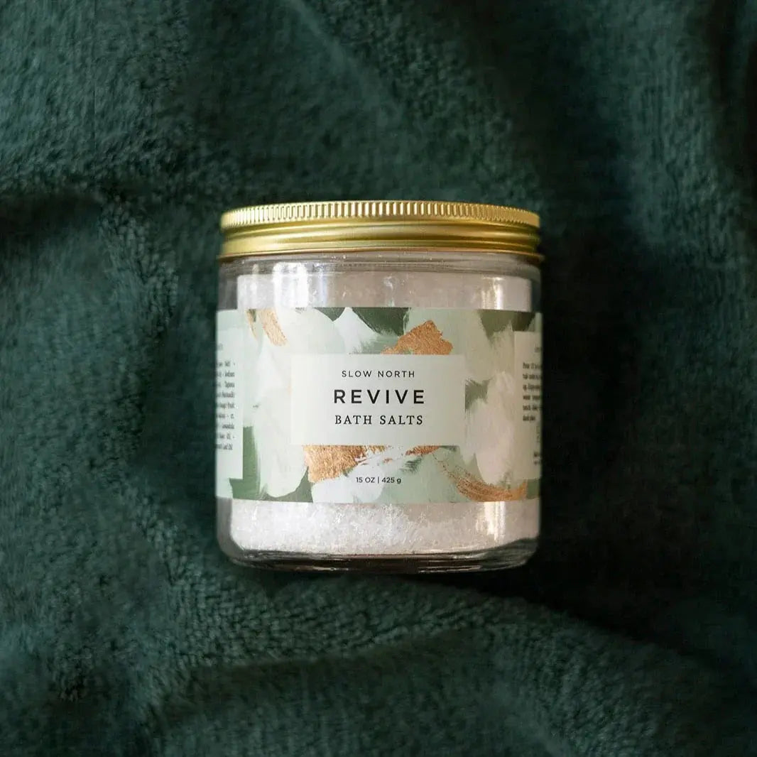 Revive bath salts in glass jar with gold lid, floral label, on cozy green towel — farmhouse spa essentials