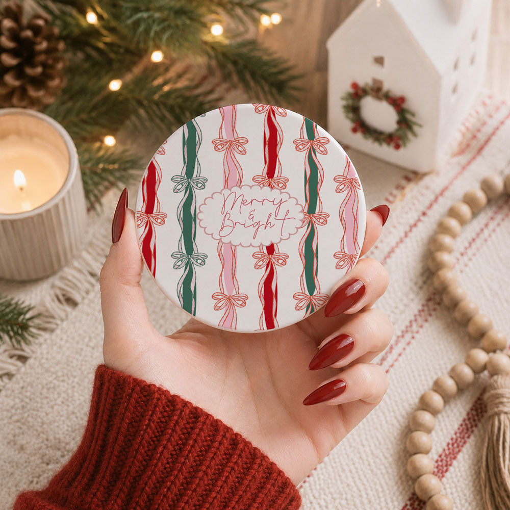 Hand holding a decorative coaster with Christmas design, surrounded by festive decor.