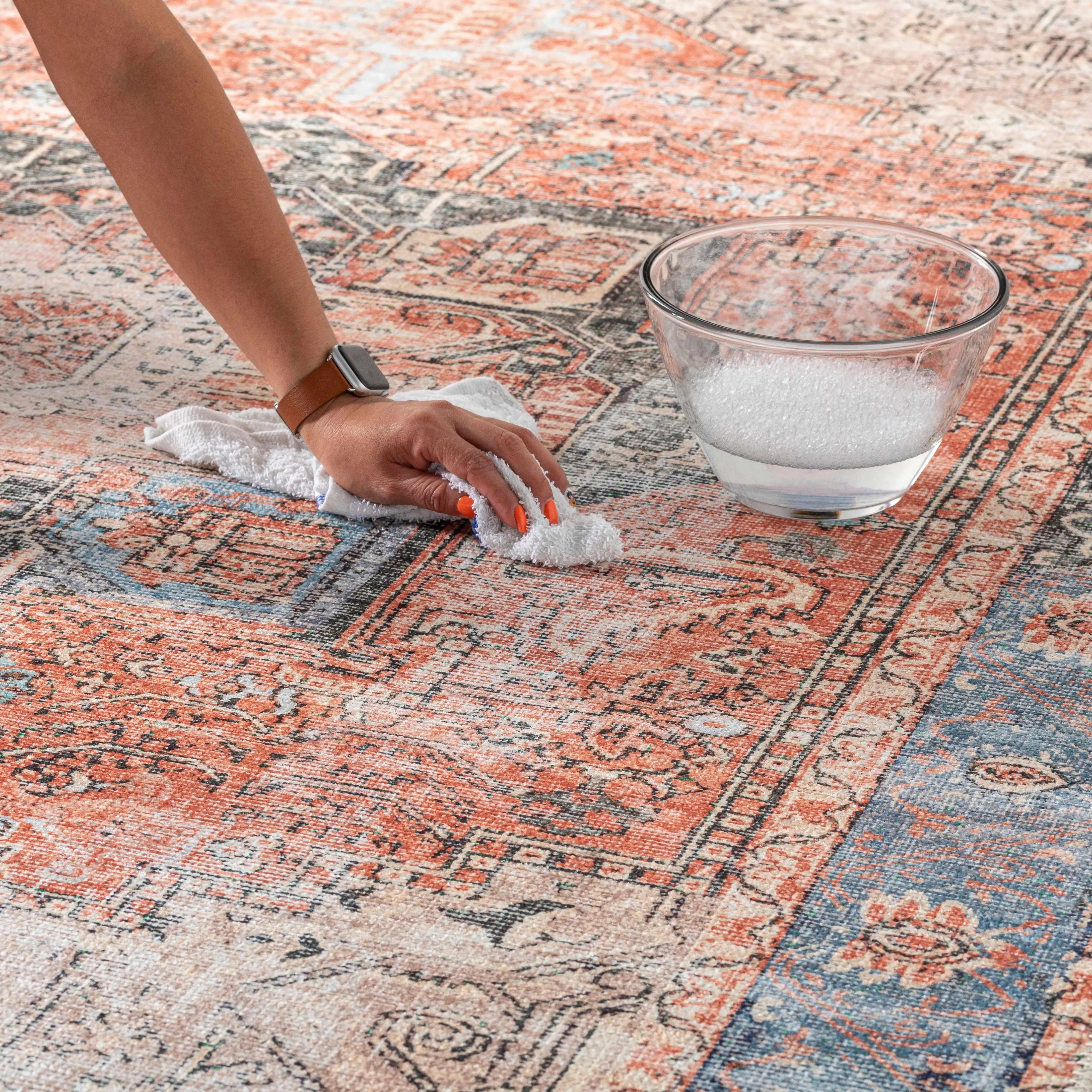 Hand cleaning patterned rug with cloth and soapy water bowl