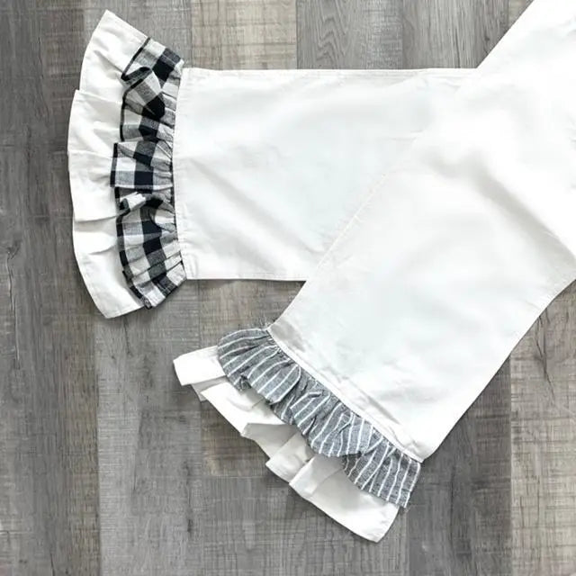 White runners laid flat on a gray wood floor, featuring black-and-white gingham plaid ruffles at one leg and gray-and-white striped ruffles at the other.
