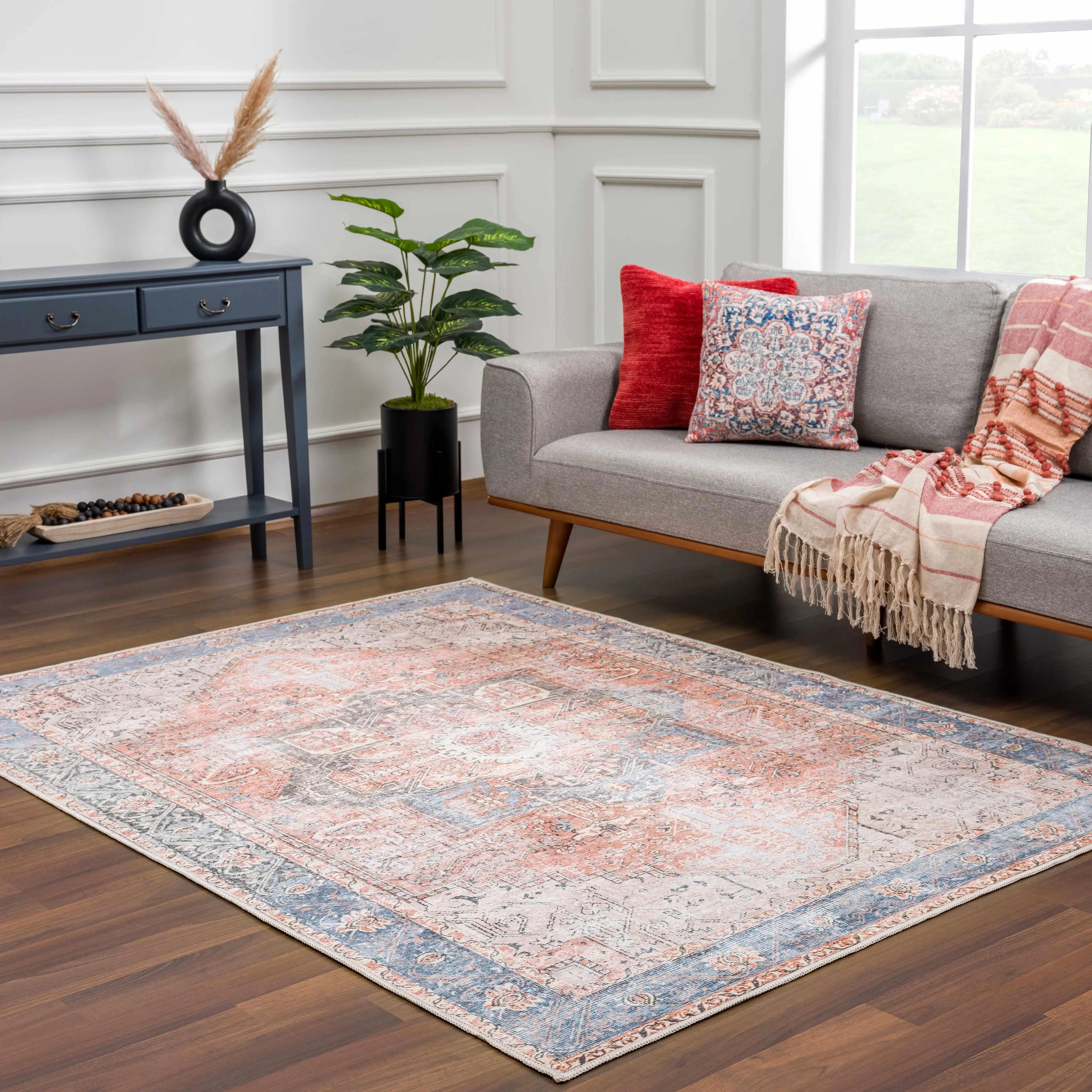 Vintage-style area rug with pink and blue boho pattern in cozy living room with gray sofa, throw pillows, and farmhouse decor.