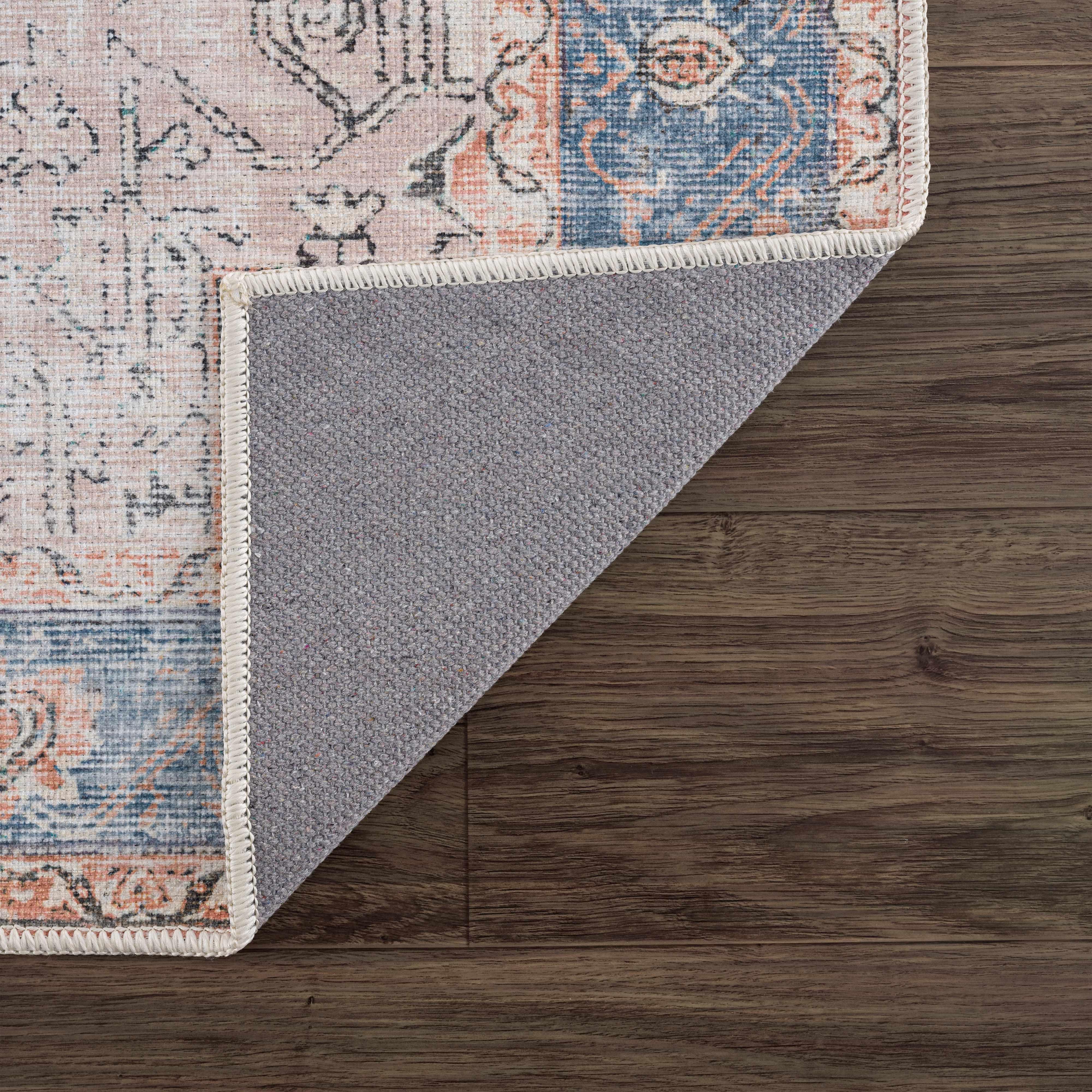 Vintage-style area rug with floral pattern, gray backing, and braided edge on wooden floor