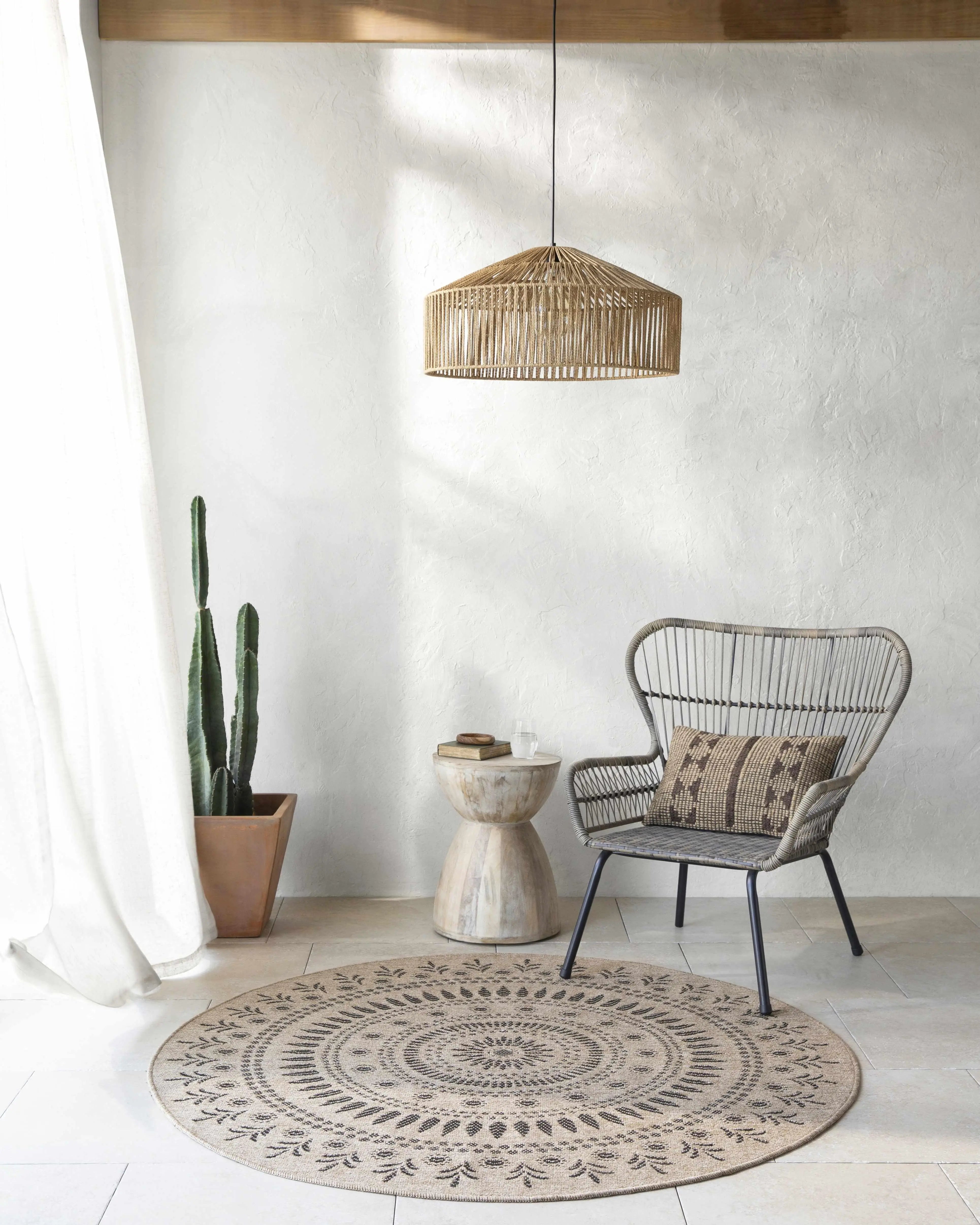 Cozy farmhouse corner with woven chair, round patterned rug, rattan pendant light, and potted cactus for warm, peaceful living spaces.