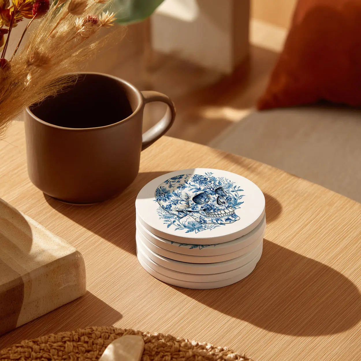 Stack of decorative coasters with a skull design next to a brown mug on a wooden surface.