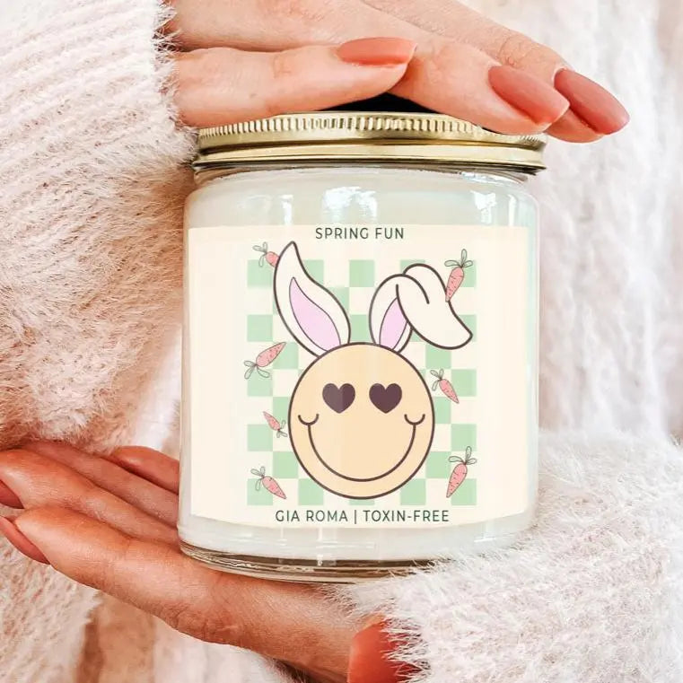Candle jar with a 'Spring Fun' label featuring bunny ears and a checkered pattern, held by a hand.