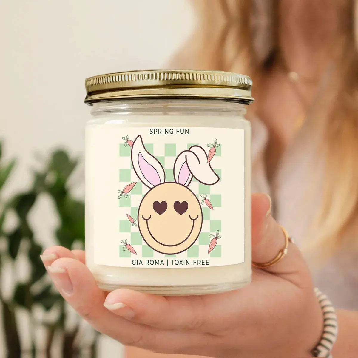 Hand holding a candle jar with a 'Spring Fun' label featuring a cartoon bunny face.