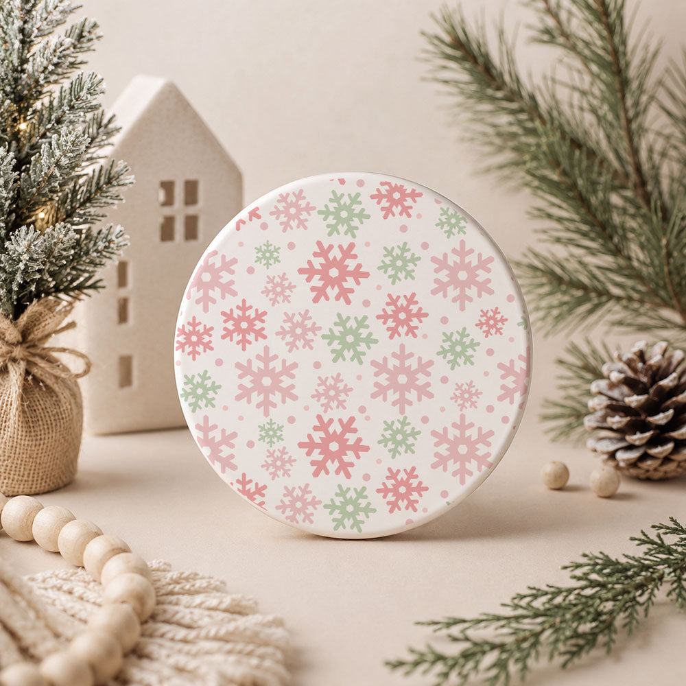 Round decorative item with pink and green snowflake pattern on a neutral background with Christmas decor.