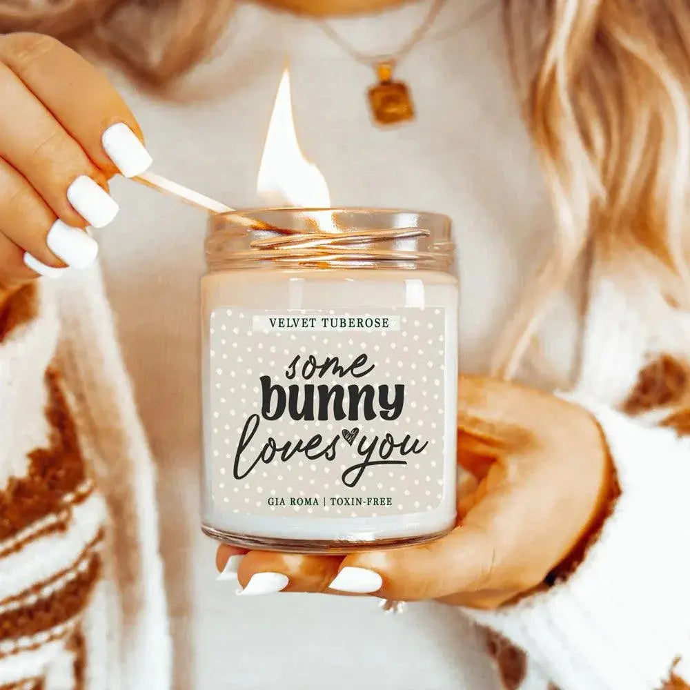 Person lighting a candle labeled 'some bunny loves you' with a soft focus background