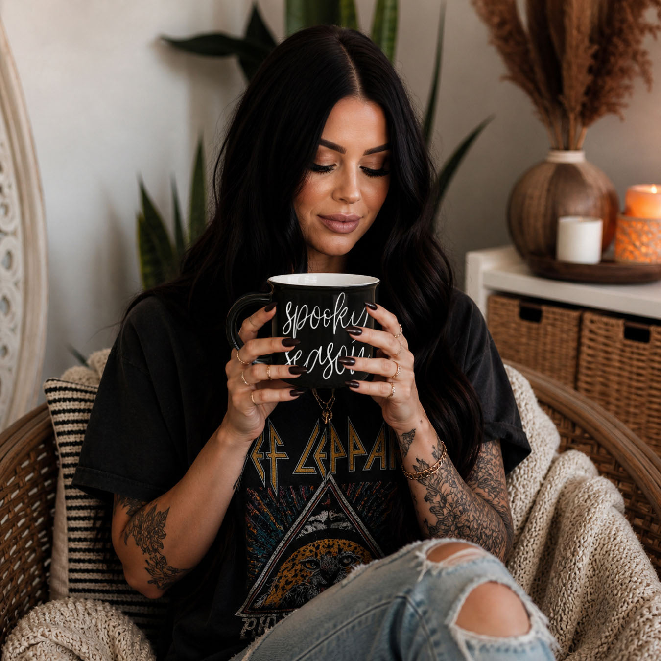 Woman holding a mug with 'Spooky Season' text, sitting in a cozy room with plants and decorative items.