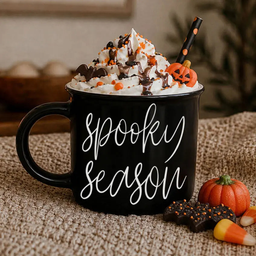 Black mug with 'Spooky Season' text, Halloween-themed whipped cream, and decorations on a textured surface.