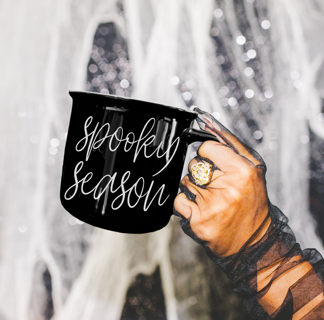 Hand holding a black mug with 'Spooky Season' text against a snowy background