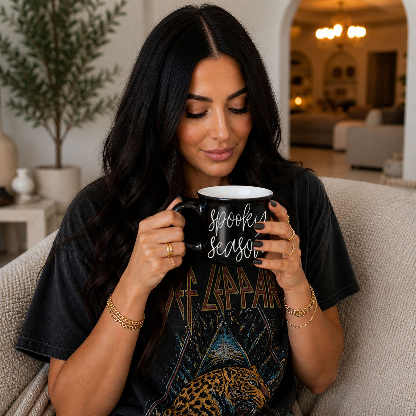 Woman holding a black mug with 'Spooky Season' text in a cozy living room.