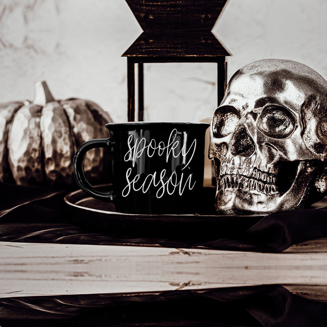 Black mug with 'Spooky Season' text, silver skull, and pumpkin on a wooden surface.