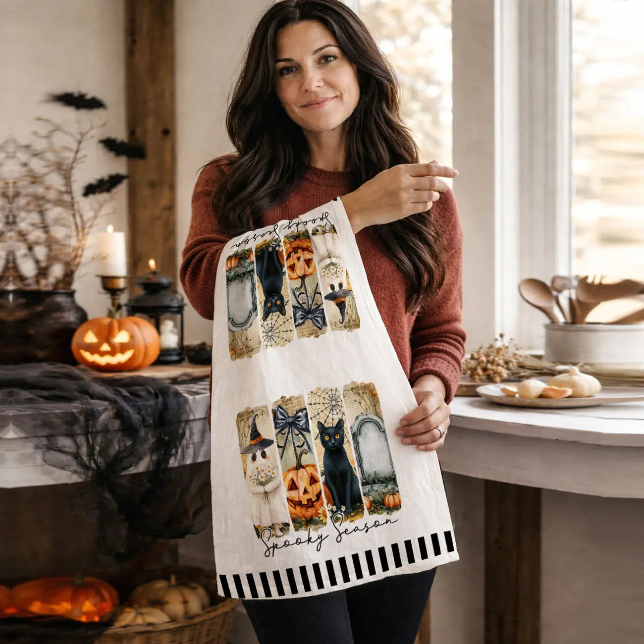 Woman holding a Halloween-themed apron in a decorated kitchen.