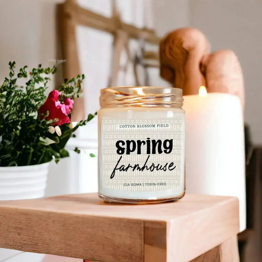 Candle labeled 'Spring Farmhouse' on a wooden surface with a blurred background