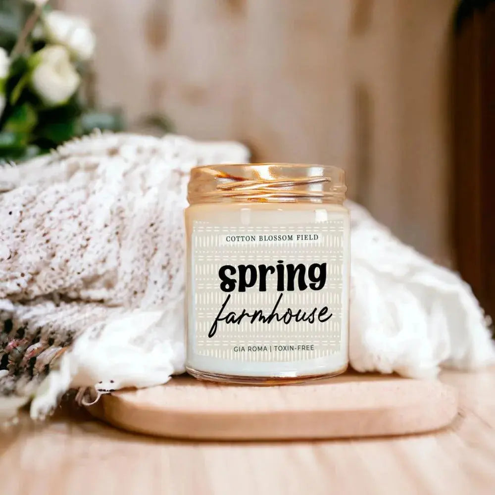 Candle labeled 'Spring Farmhouse' on a wooden surface with a soft blurred background