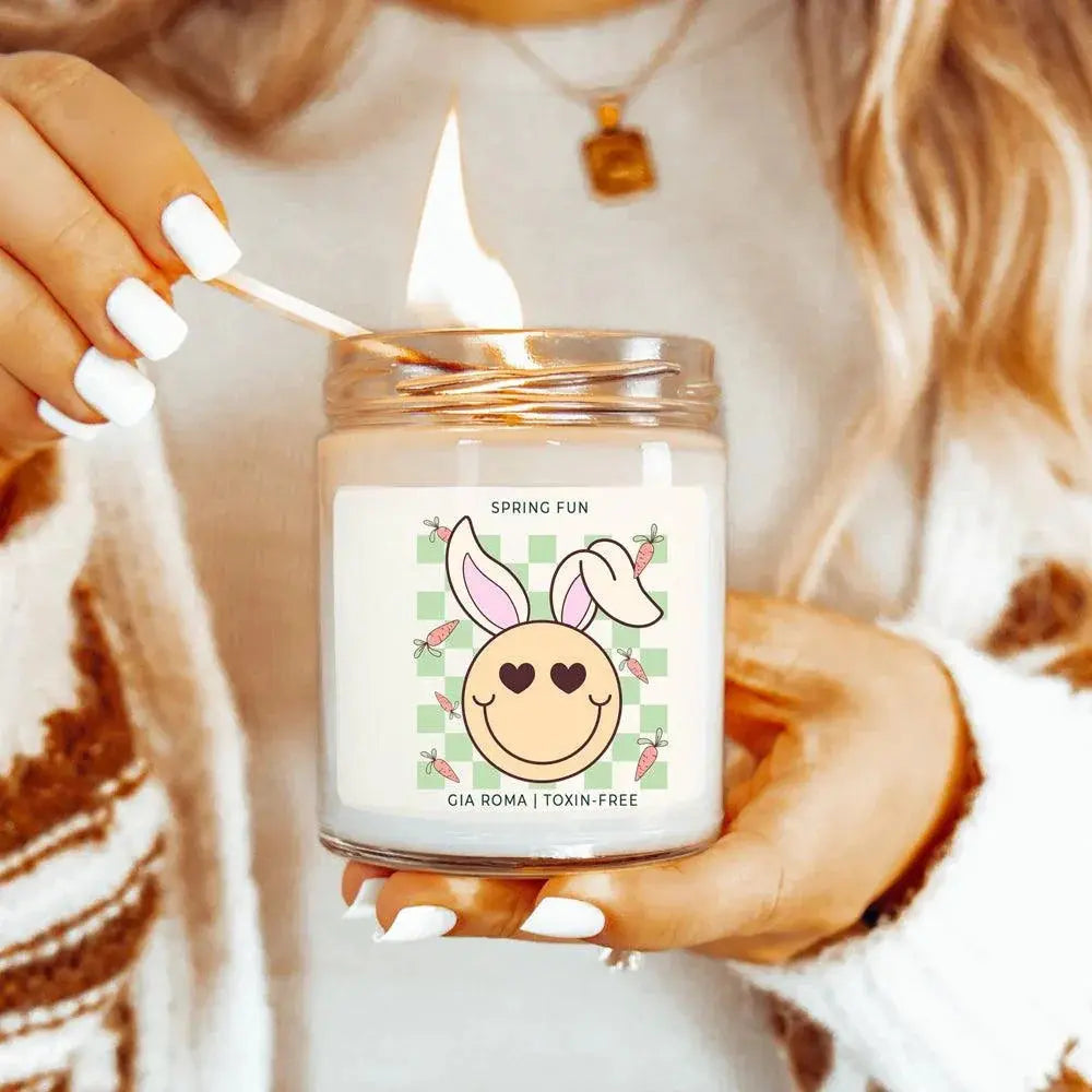Person holding a candle with a decorative label featuring a cartoon face and bunny ears.