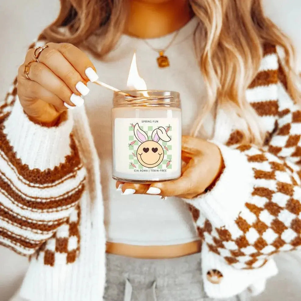 Person lighting a candle with a smiley face design, wearing a patterned sweater.