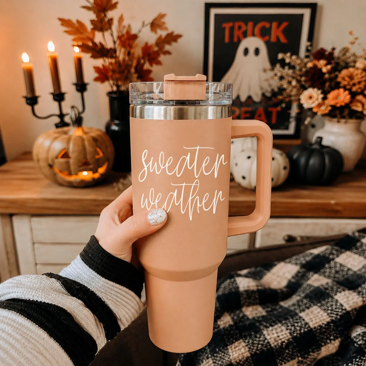 Person holding a 'Sweater weather' travel mug with Halloween decorations in the background
