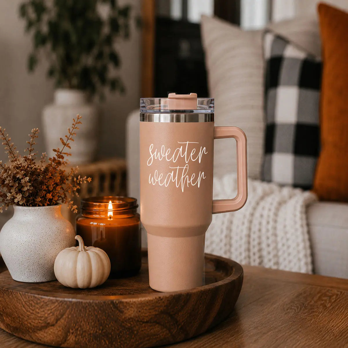 Travel mug with 'sweater weather' text on a wooden table with decorative items.