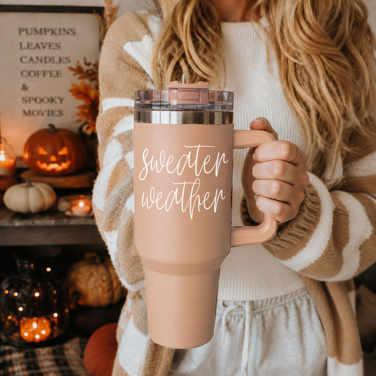 Person holding a 'sweater weather' mug with Halloween decorations in the background