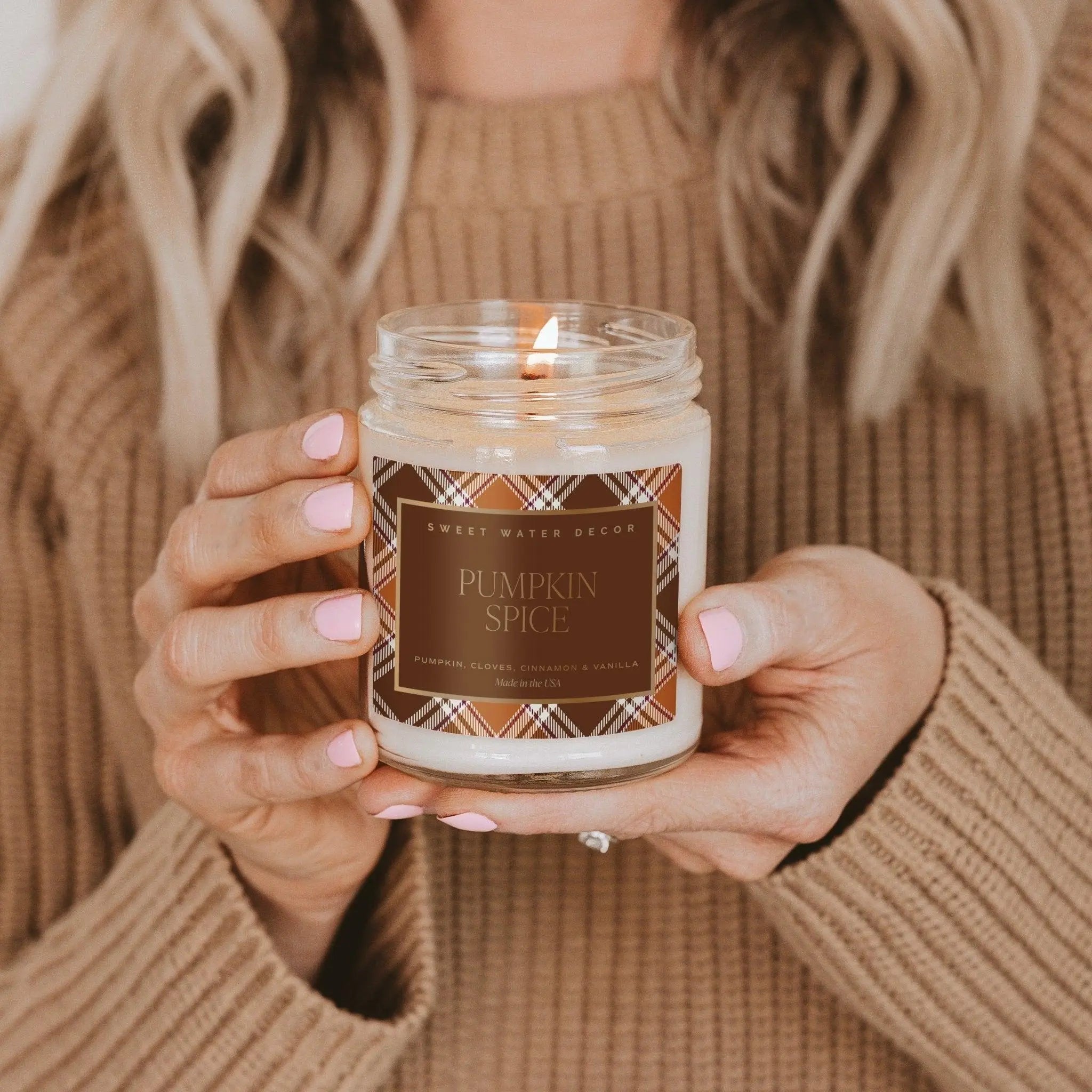 Person holding a 'Pumpkin Spice' candle with a plaid label.