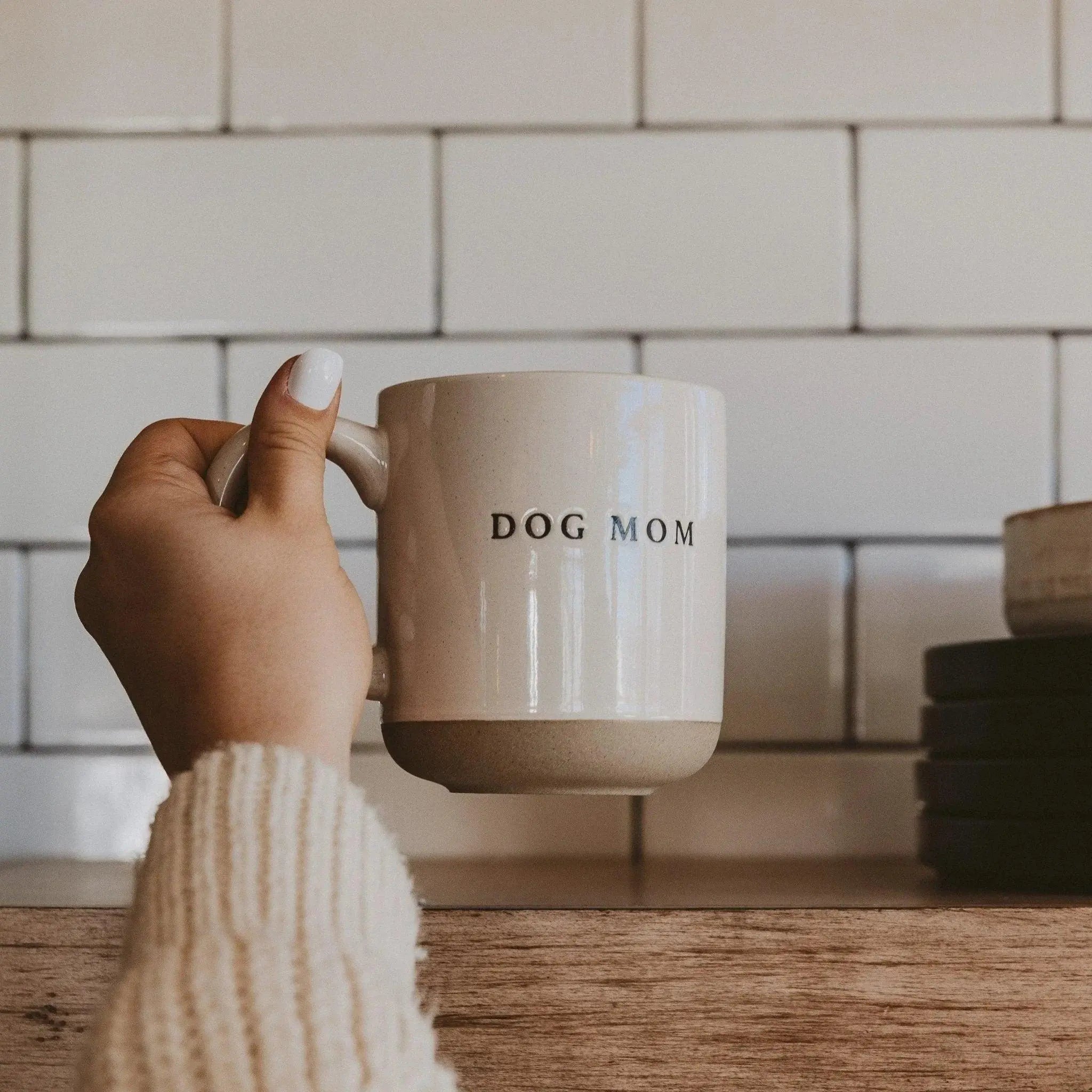 Hand holding 'Dog Mom' ceramic mug in cozy farmhouse kitchen, perfect for coffee lovers and pet parents.