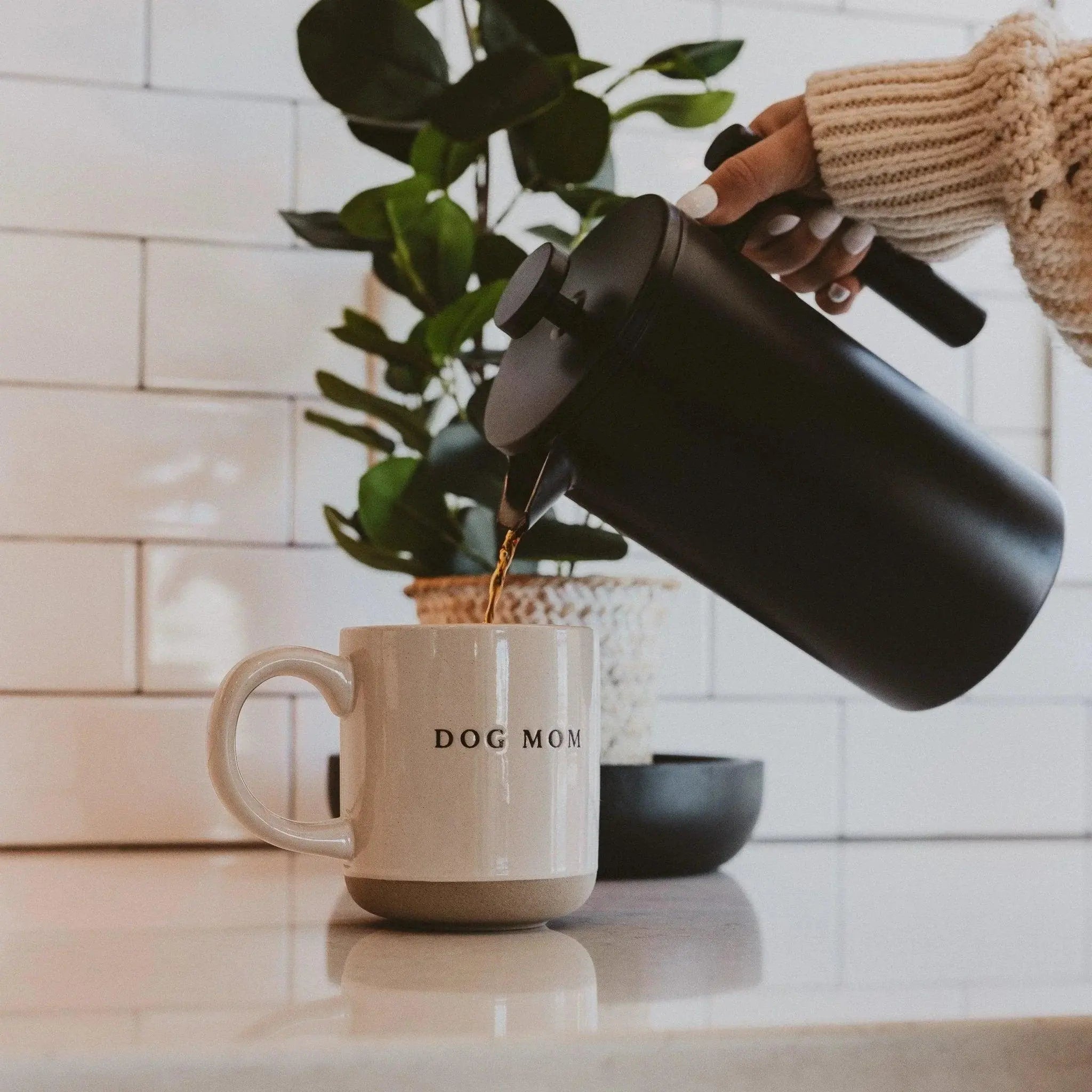 Cozy kitchen scene with 'Dog Mom' mug, pouring coffee from black carafe, farmhouse decor style