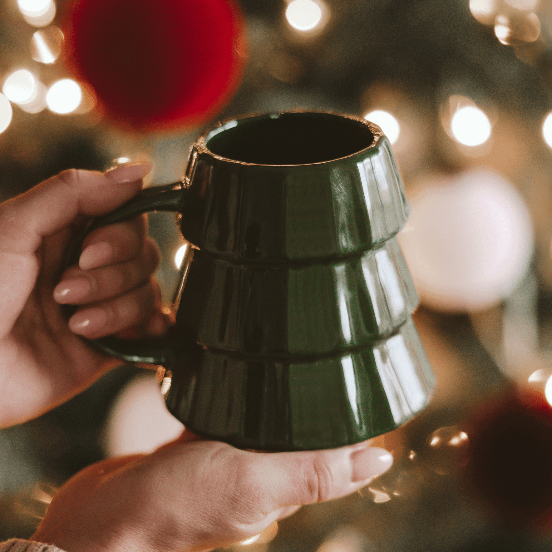 Green mug held by hands with festive lights in the background