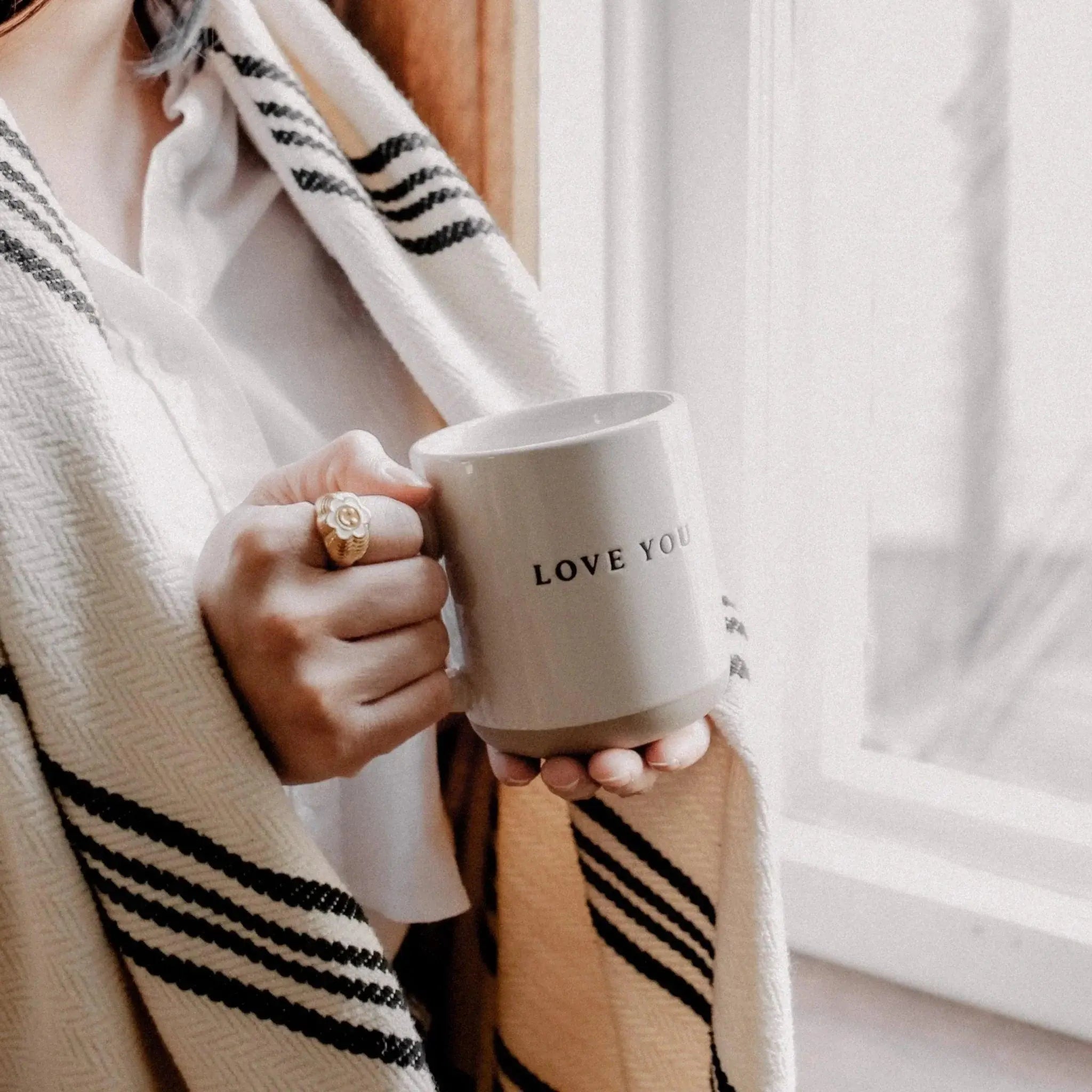 Cozy farmhouse mug with 'LOVE YOU' text, held by person in striped robe near window