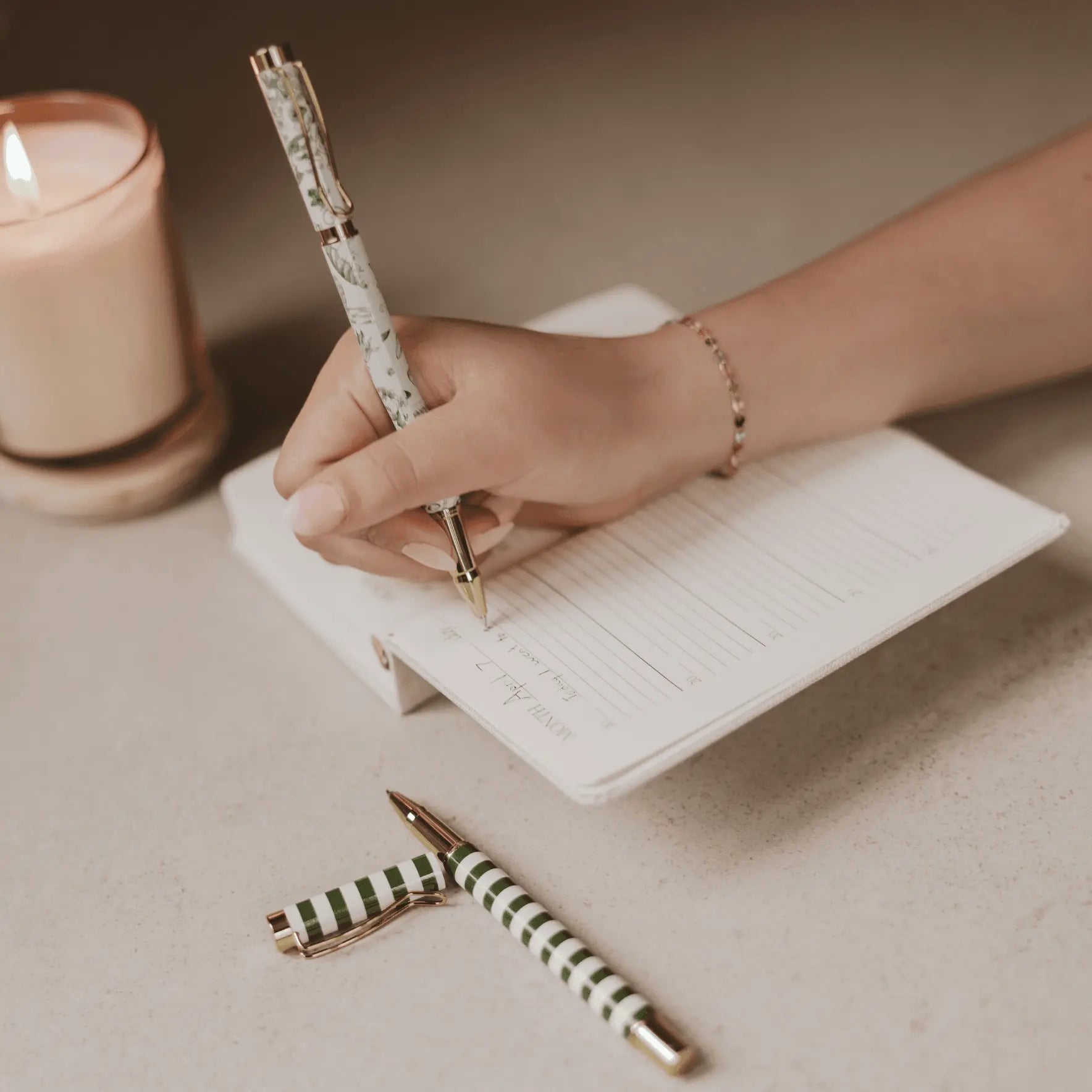 Hand holding a pen over a notebook with a lit candle in the background
