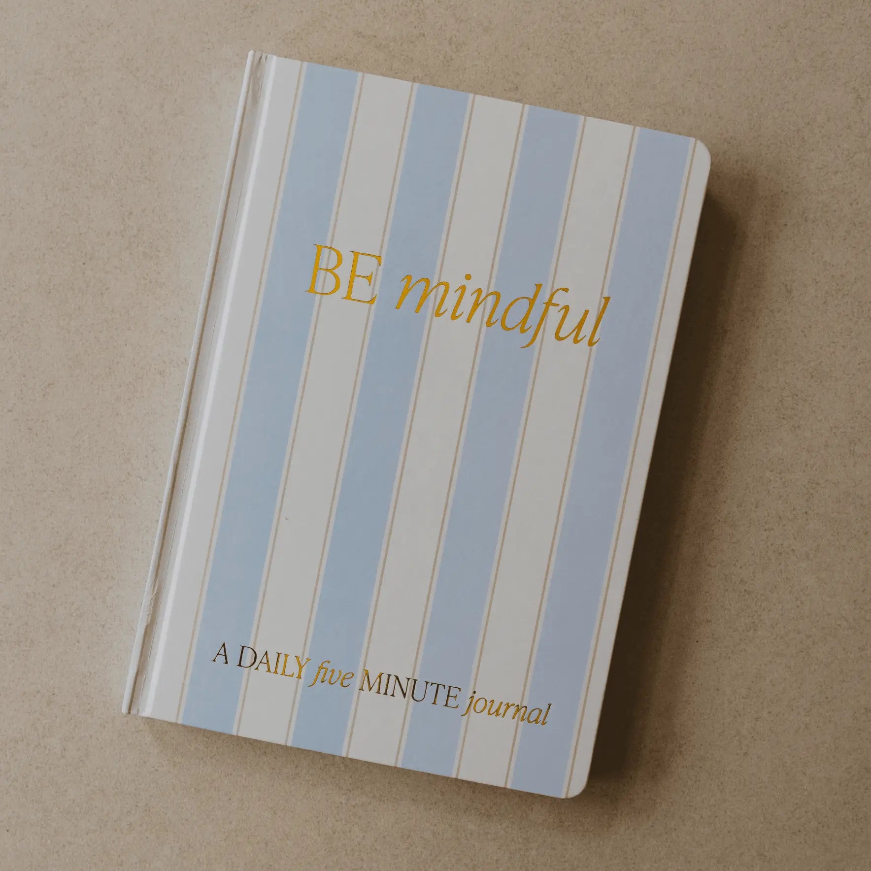 Journal with blue and white striped cover and 'BE mindful' text on a beige background