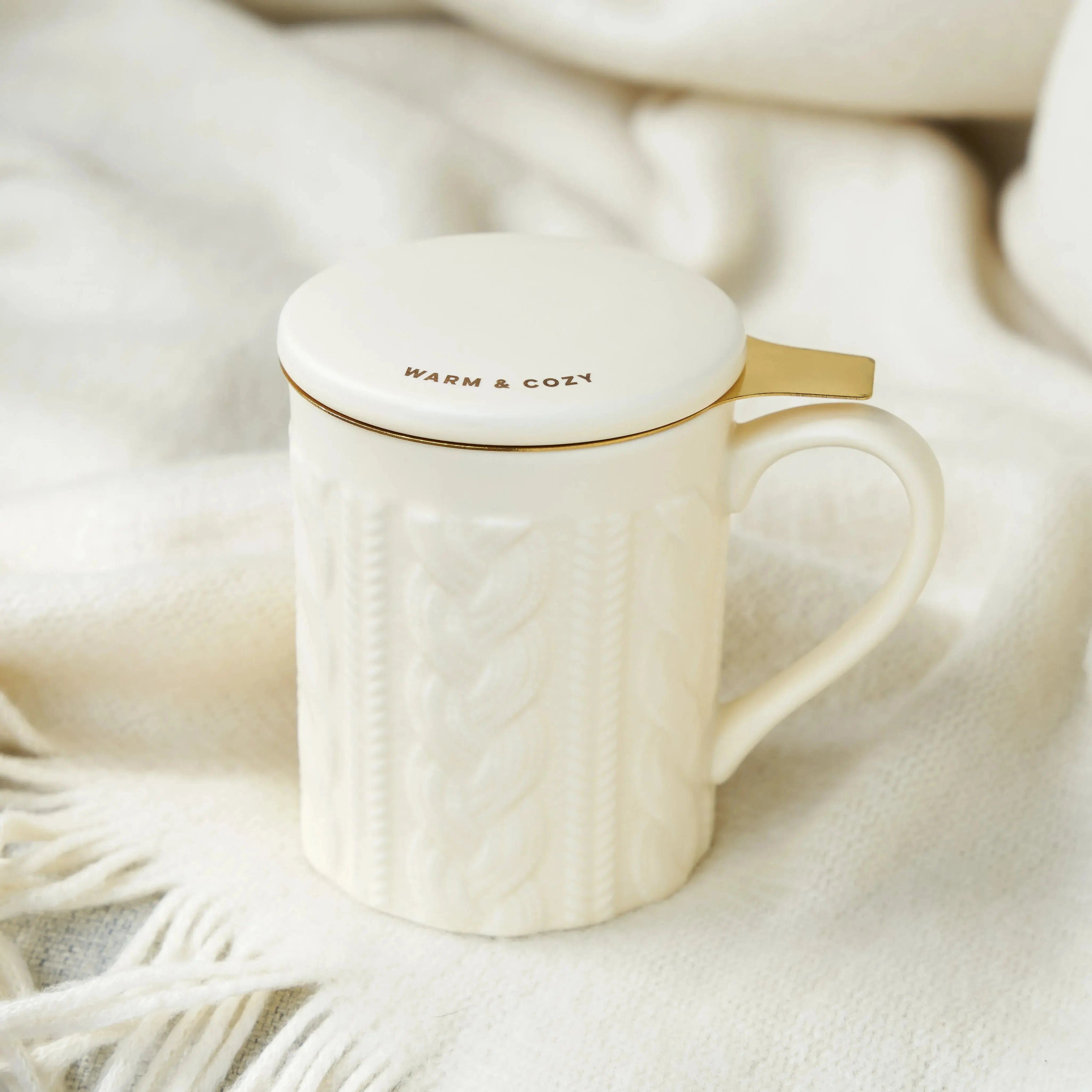 White mug with gold handle and 'Warm & Cozy' lid on a soft white background