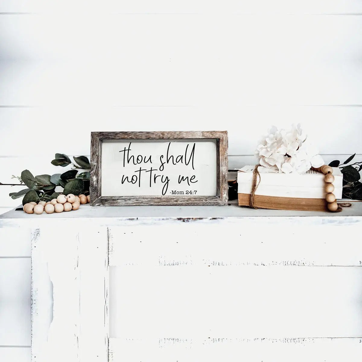 Decorative sign with ' Thou shall not try me' text on a white surface with decorative items.