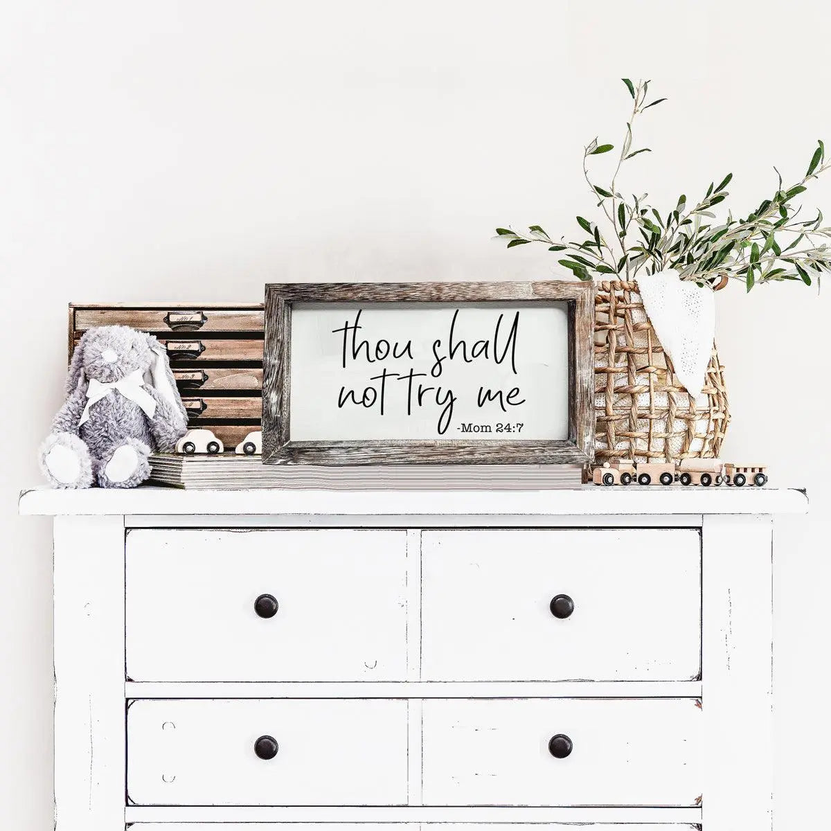 White dresser with decorative items including a framed quote, a stuffed bunny, and a plant.