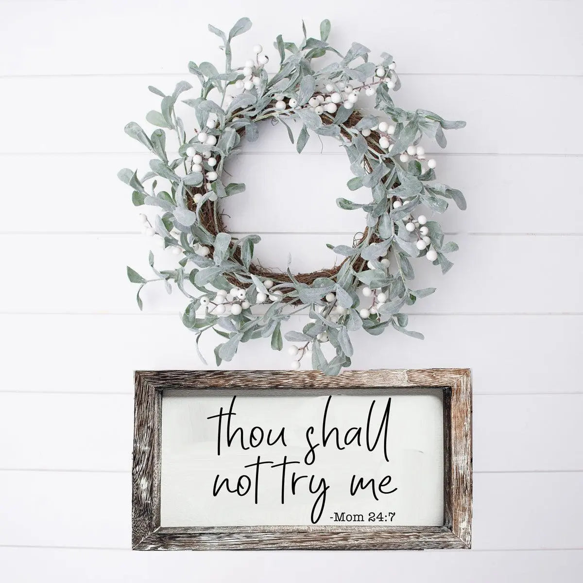 Wreath with greenery and a framed sign with text on a white wooden background