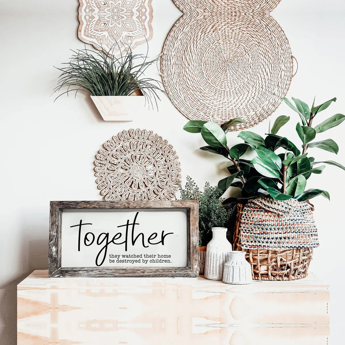 Decorative wall with plants, woven baskets, and a framed sign on a wooden surface.