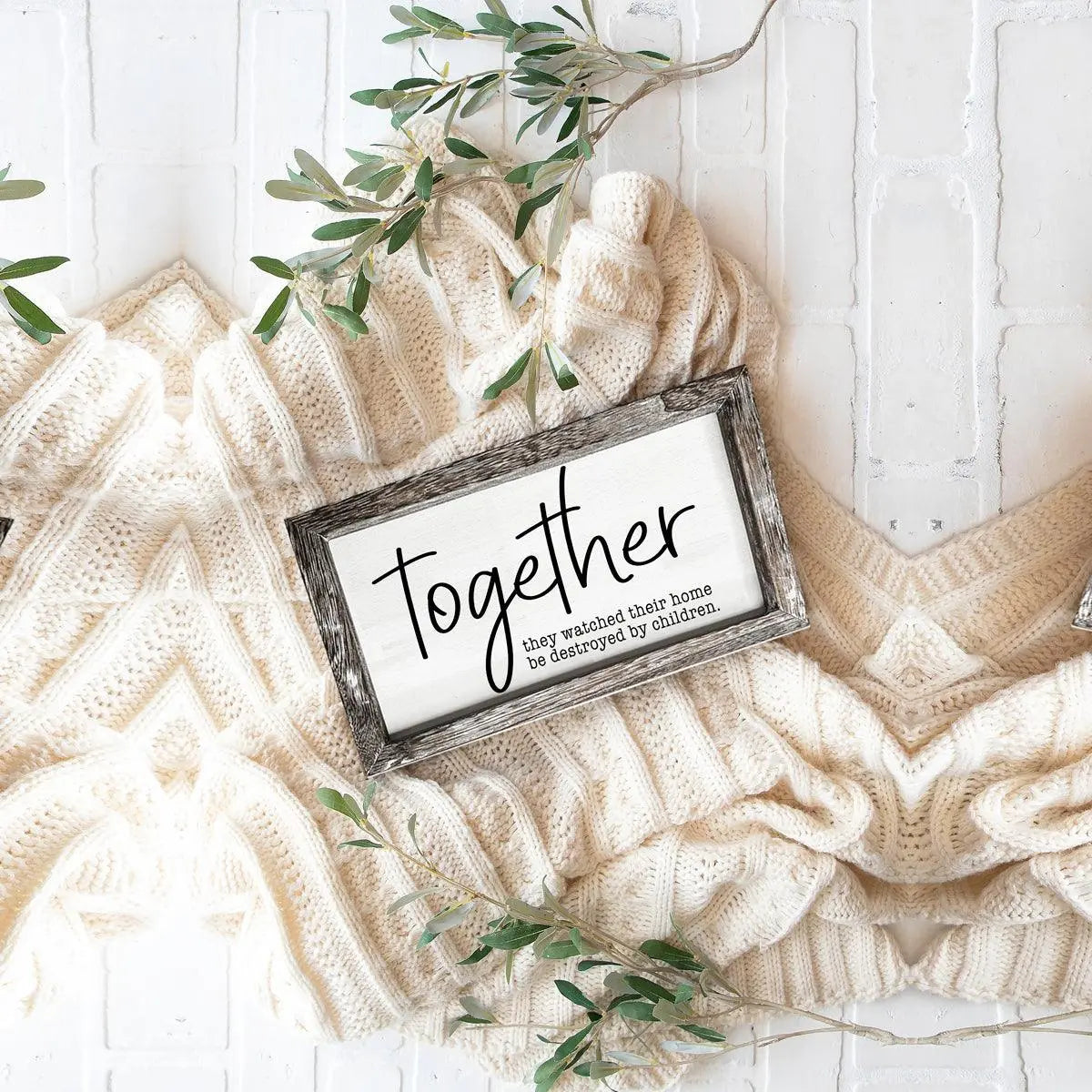 Framed sign with 'Together' text on a textured surface with greenery