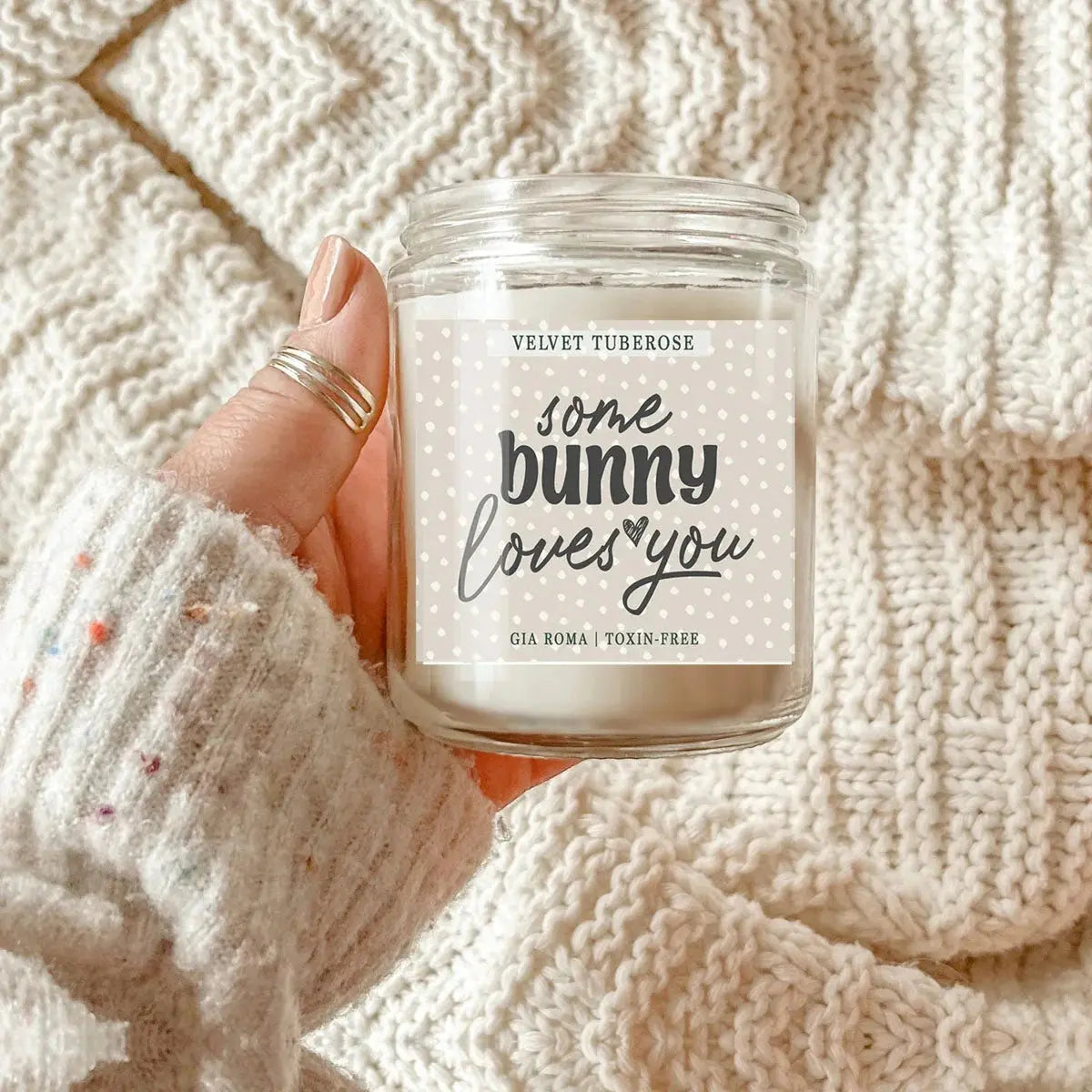Candle labeled 'some bunny loves you' held against a textured beige background