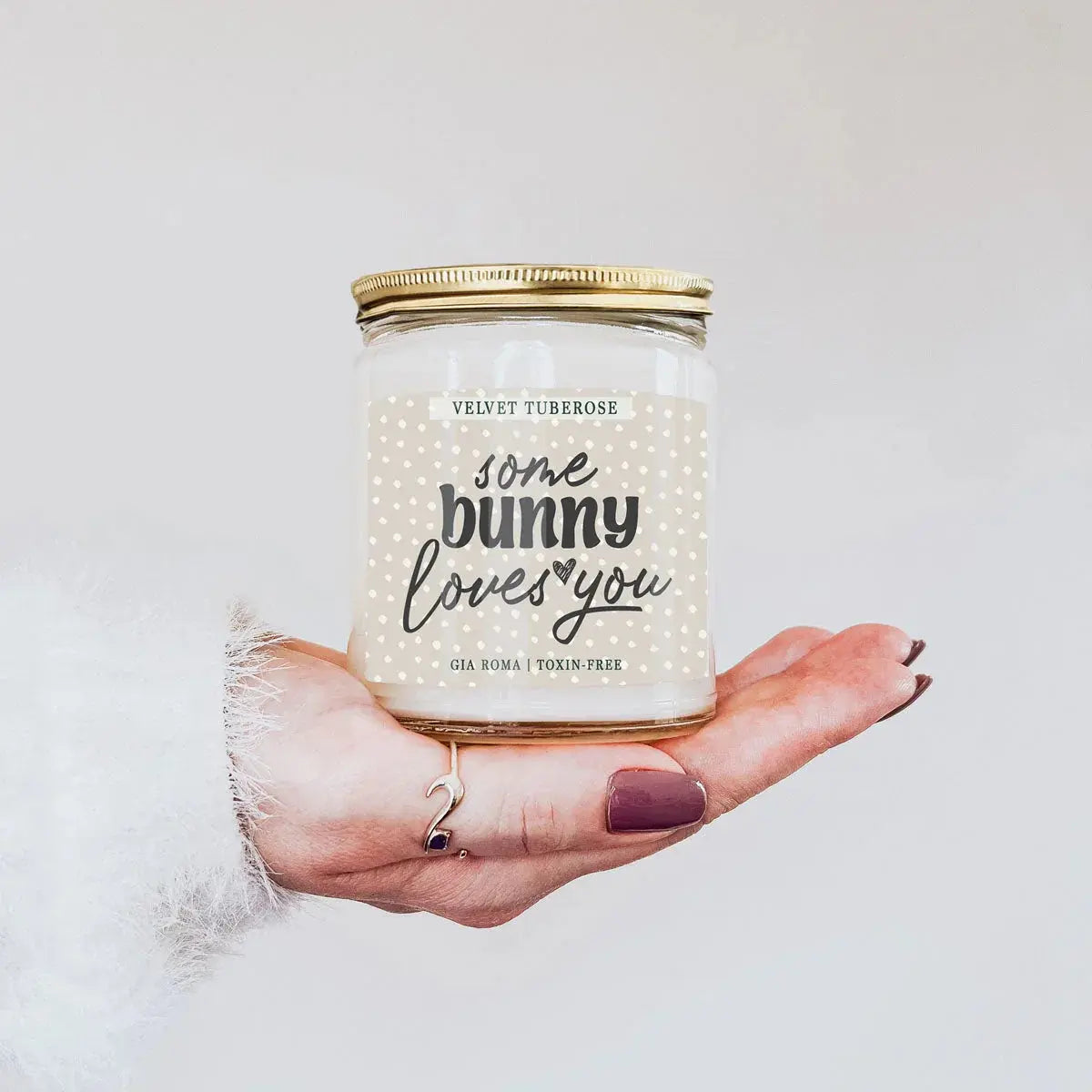 Candle jar labeled 'some bunny loves you' held in a hand against a light background