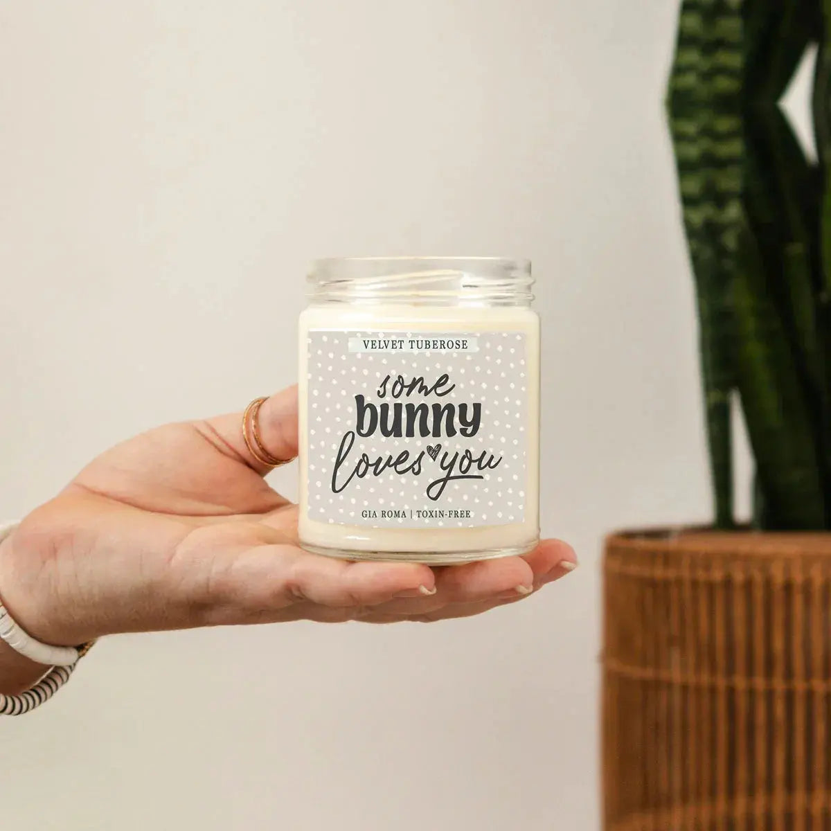 Hand holding a candle labeled 'some bunny loves you' with a plant in the background